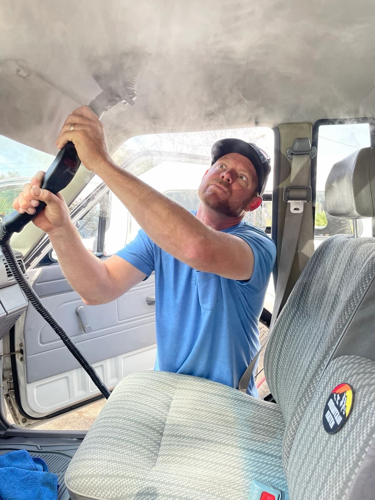 Detailer steam cleaning the headliner and seats inside a vehicle